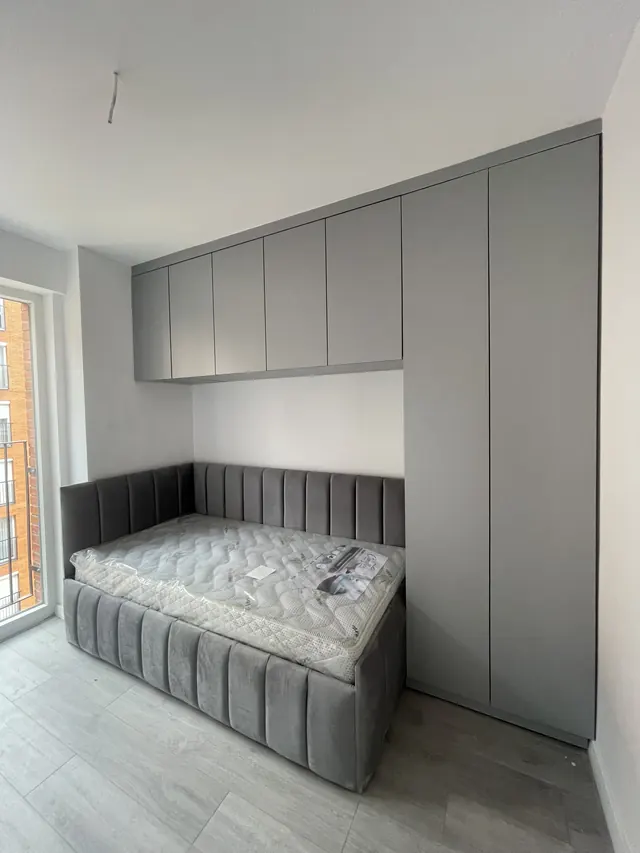 Gepolstertes Bett mit Überbauschrank und grauen Hochschränken