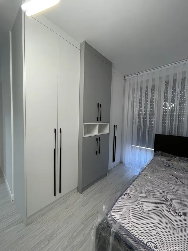 Weiß-grauer Kleiderschrank mit offenem Fach neben einem Bett