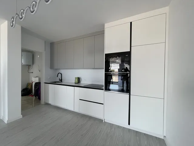 Weiße Küchenzeile mit schwarzen Griffleisten und Backofen im Hochschrank