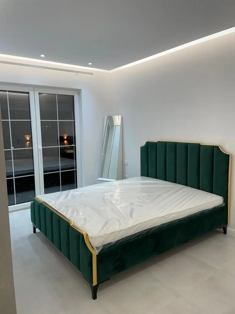 Grünes Polsterbett mit goldenem Rahmen in einem hellen Schlafzimmer