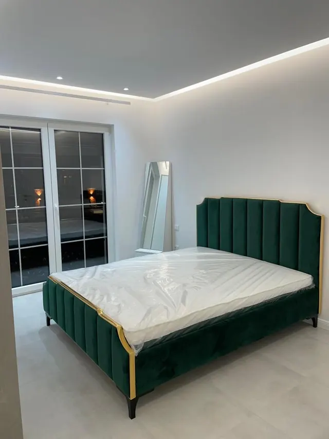 Grünes Polsterbett mit goldenem Rahmen in einem hellen Schlafzimmer