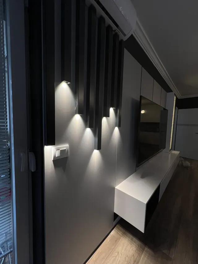 Dunkle TV-Wand mit Lamellen, Wandleuchten und schwebendem Lowboard