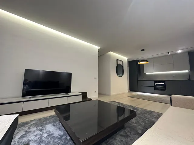Wohnzimmer mit weißem TV-Lowboard und offener Küche im Hintergrund